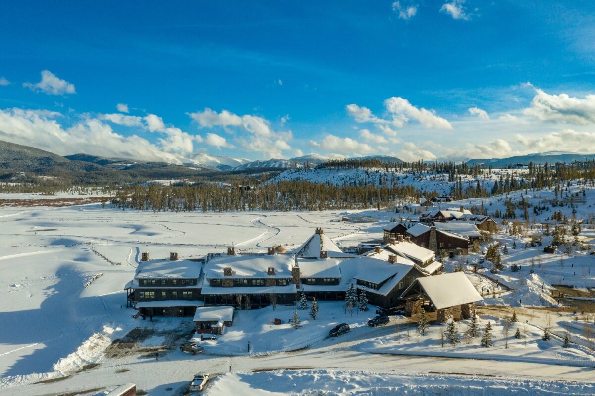 Aerial view of a snowy mountain resort with buildings and vehicles surrounded by trees and mountains in Grand County Colorado.