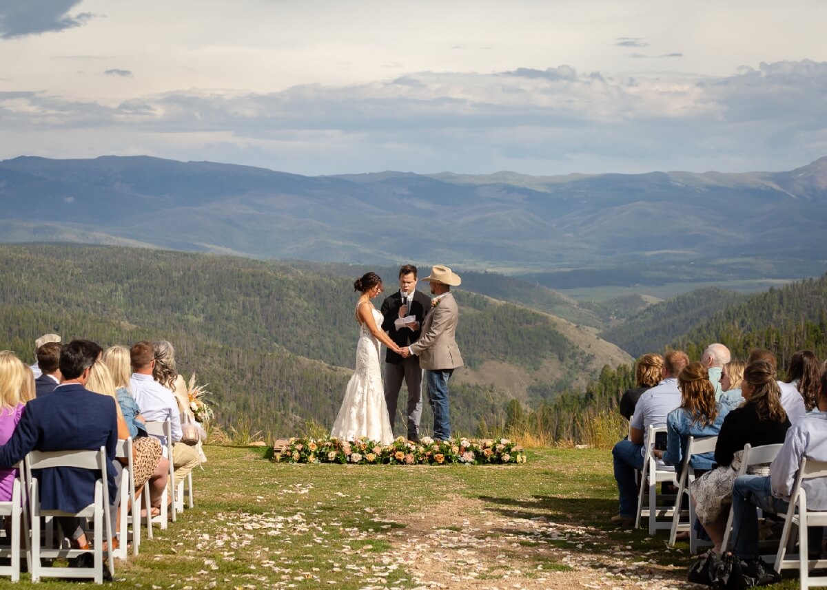 A couple exchanges vows on a mountain top, surrounded by guests and a breathtaking view in Grand County Colorado.