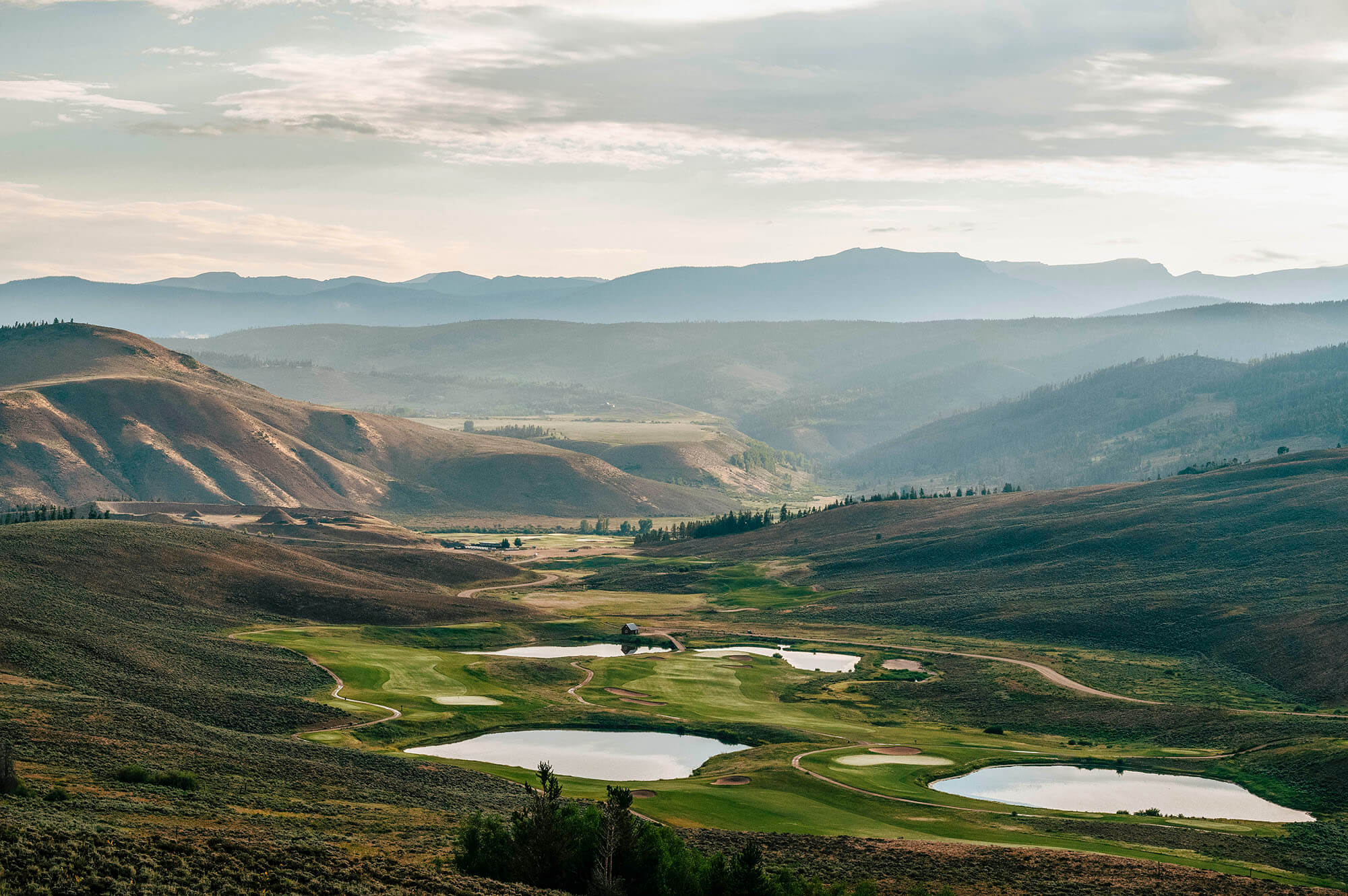 Aerial view of a serene valley with winding rivers, lush green fields, and distant mountains in Grand County Colorado.