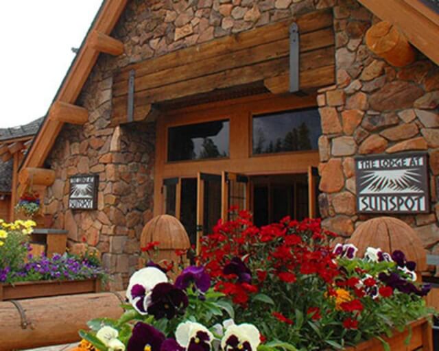 A rustic stone building with a wooden sign reading 'Sunspot' and colorful flower beds in Grand County Colorado.