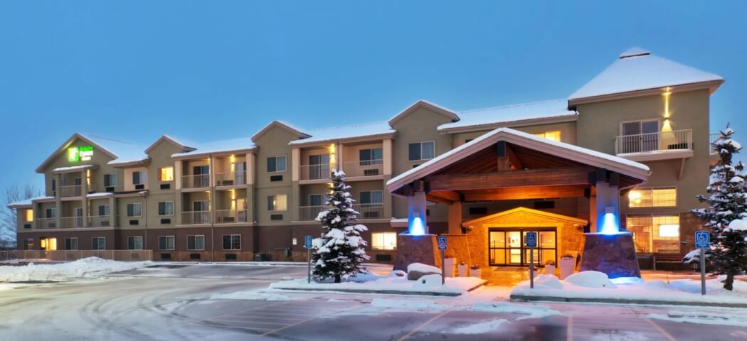 A snow-covered hotel with a lit entrance and balconies, surrounded by evergreen trees in Grand County Colorado.
