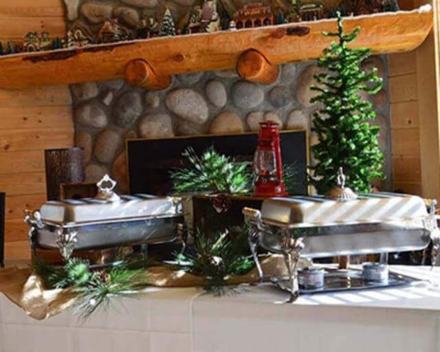 A festive table setting with chafing dishes, pine decorations, and a Christmas tree near a stone fireplace in Grand County Colorado.