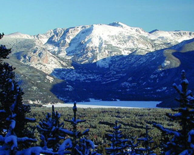 Snow-capped mountain range with evergreen trees and frozen lake in the foreground in Grand County Colorado.