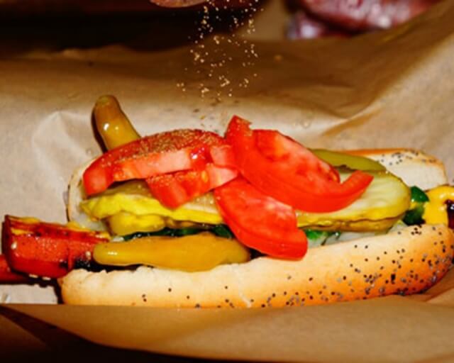 A hot dog topped with tomatoes, pickles, peppers, and mustard in a poppy seed bun in Grand County Colorado.
