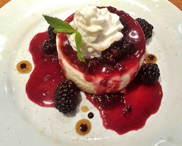 A creamy cheesecake topped with whipped cream, blackberries, and a red berry sauce in Grand County Colorado.