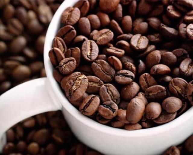 A white mug brimming with dark brown coffee beans, some split open in Grand County Colorado.