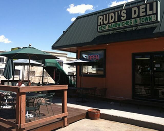 A person sits on a deck outside a deli with a sign advertising sandwiches in Grand County Colorado.