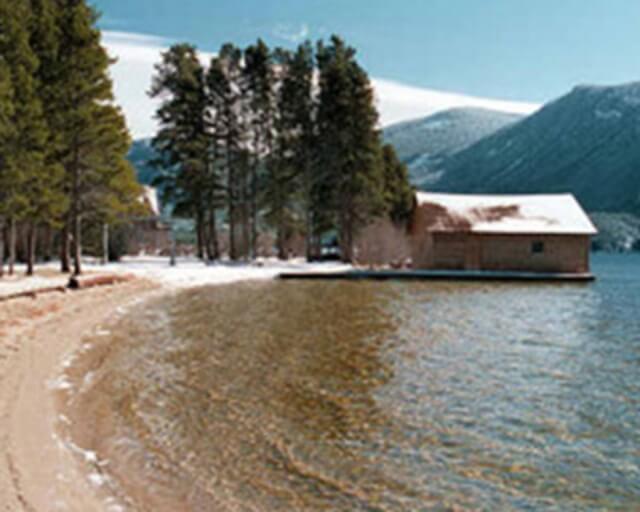 A serene winter lakeside scene with snow-covered trees and a small cabin on the shore in Grand County Colorado.