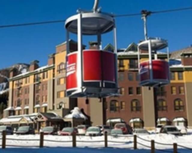 Aerial gondola lifts transport skiers over snow-covered ground near mountain resort buildings in Grand County Colorado.