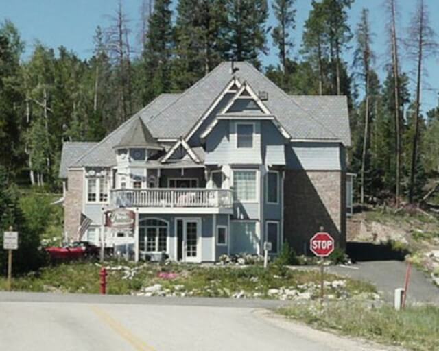 A large, multi-story house with a gray roof and white siding is nestled among tall trees in Grand County Colorado.