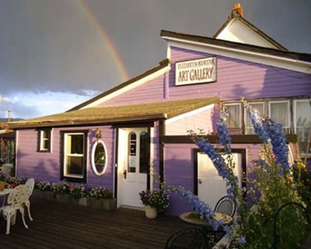 A charming purple art gallery with a rainbow overhead and a cozy outdoor seating area in Grand County Colorado.