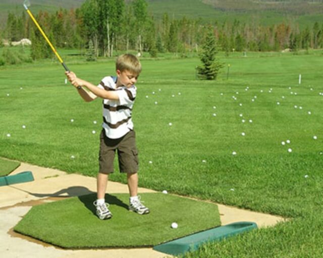 A young boy practices his golf swing on a driving range with multiple golf balls around him in Grand County Colorado.