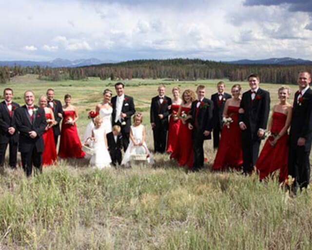 A wedding party in red and black formal attire poses outdoors with mountains in the background in Grand County Colorado.