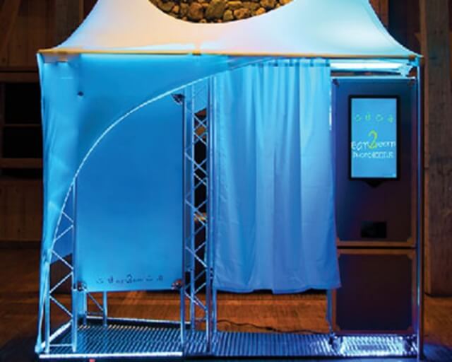 A blue-lit photo booth with a curved roof and a curtain inside in Grand County Colorado.
