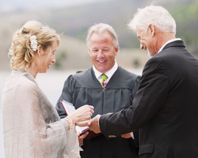 A wedding ceremony with a bride, groom, and officiant exchanging rings outdoors in Grand County Colorado.