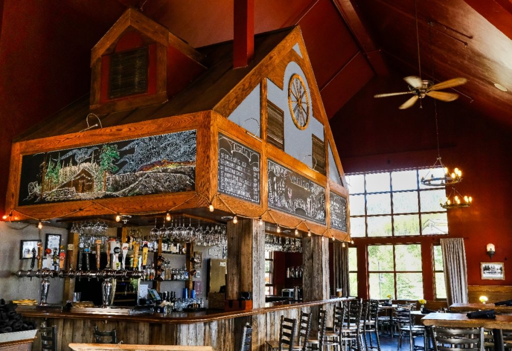 Rustic bar with wooden interior, chalkboard menu, and large windows overlooking a scenic view in Grand County Colorado.