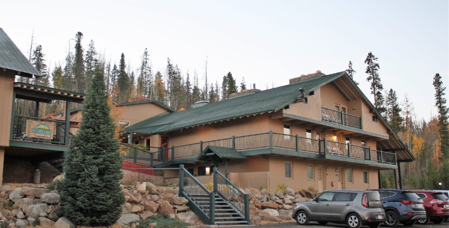A rustic, multi-story lodge with balconies and a staircase, nestled among tall trees in Grand County Colorado.
