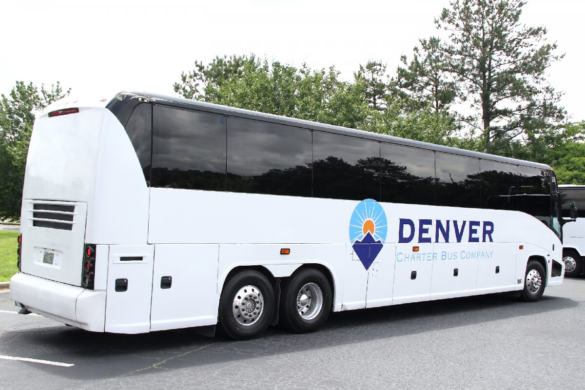 A white Denver Charter Bus Company bus with blue and orange logo parked outdoors in Grand County Colorado.