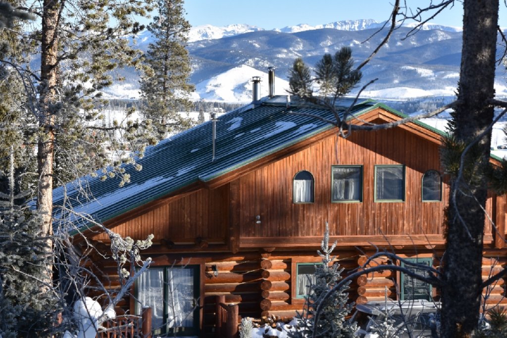 A rustic log cabin nestled among snow-covered trees with a view of distant mountains in Grand County Colorado.