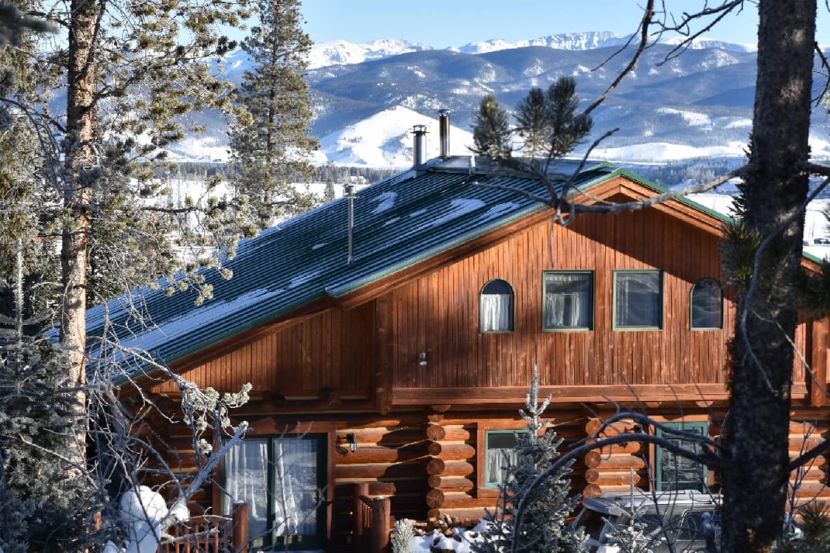 A rustic log cabin nestled among snow-covered trees with a view of distant mountains in Grand County Colorado.