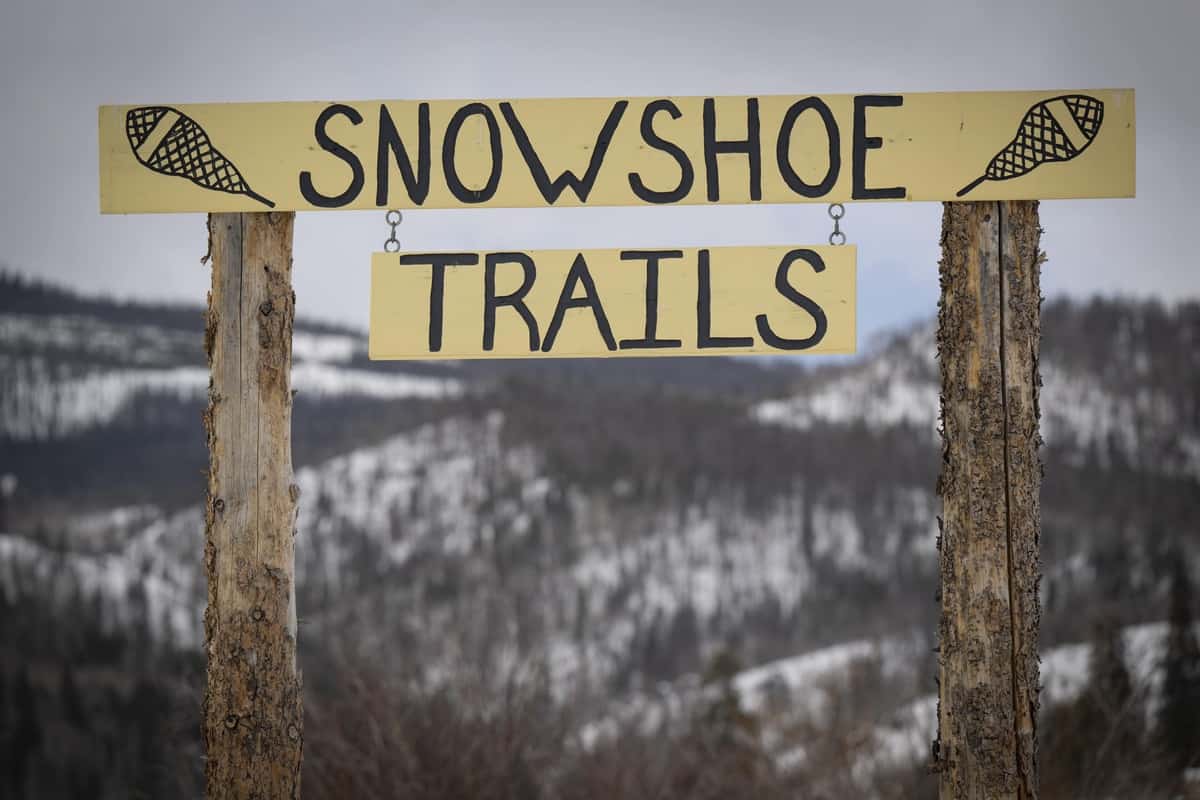 A sign that says "snowshoe trails" with the Rocky Mountains in the background