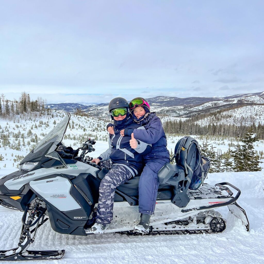 Two people sitting on a snowmobile in the snow.