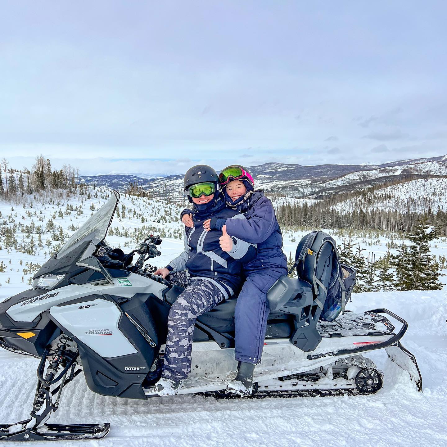 Two people sitting on a snowmobile in the snow.