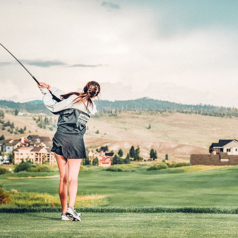 A woman swinging a golf club on a golf course.