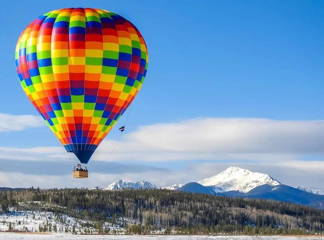 A colorful hot air balloon flying over a snowy field with mountains in the background.