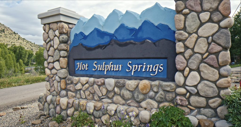 A stone sign with a mountain backdrop marks the entrance to Hot Sulphur Springs in Grand County Colorado.