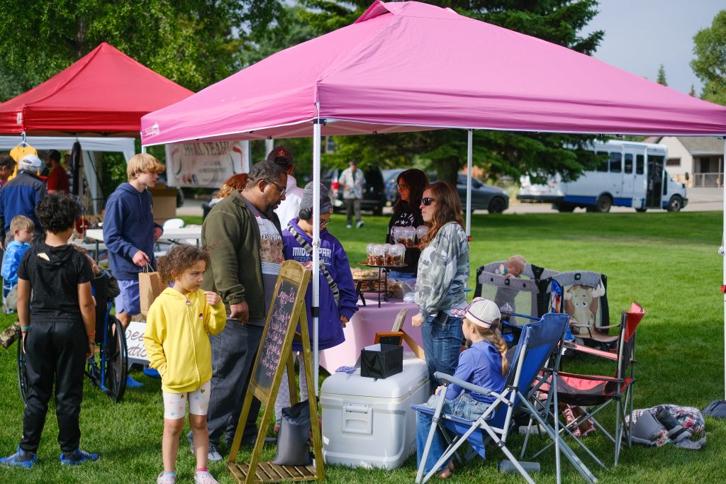Family shopping at a Granby farmers market with vendors under pink and red tents.