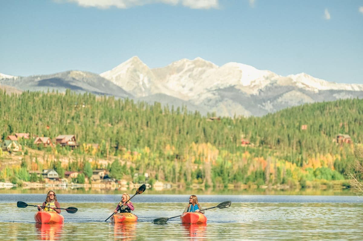 Three people kayaking on Grand Lake, Colorado, with stunning mountain views of Rocky Mountain National Park in the background.