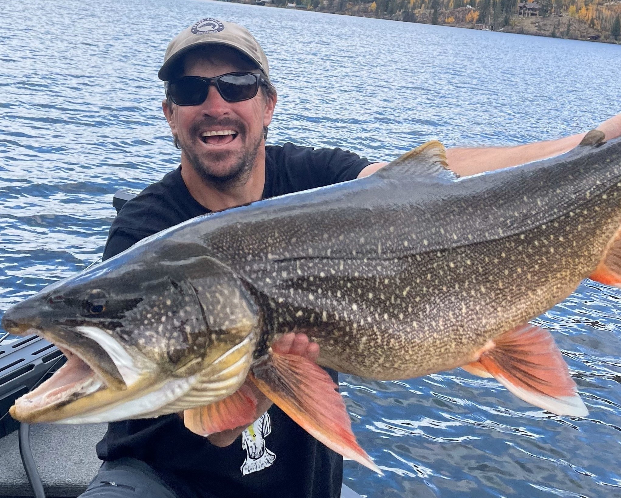 Man proudly displays a large, spotted fish with orange fins on a boat in Grand County Colorado.