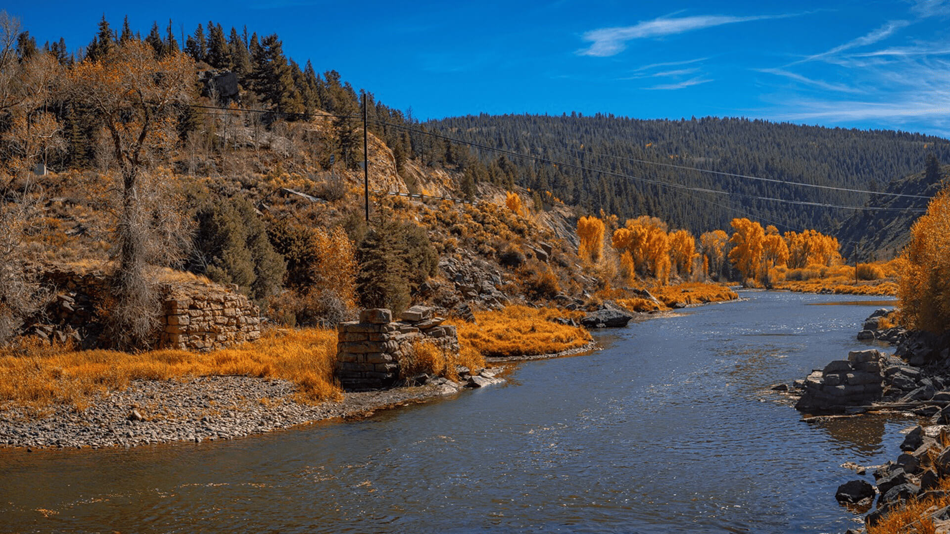 A winding river flows through a canyon with autumn-colored trees and rocky cliffs in Grand County Colorado.