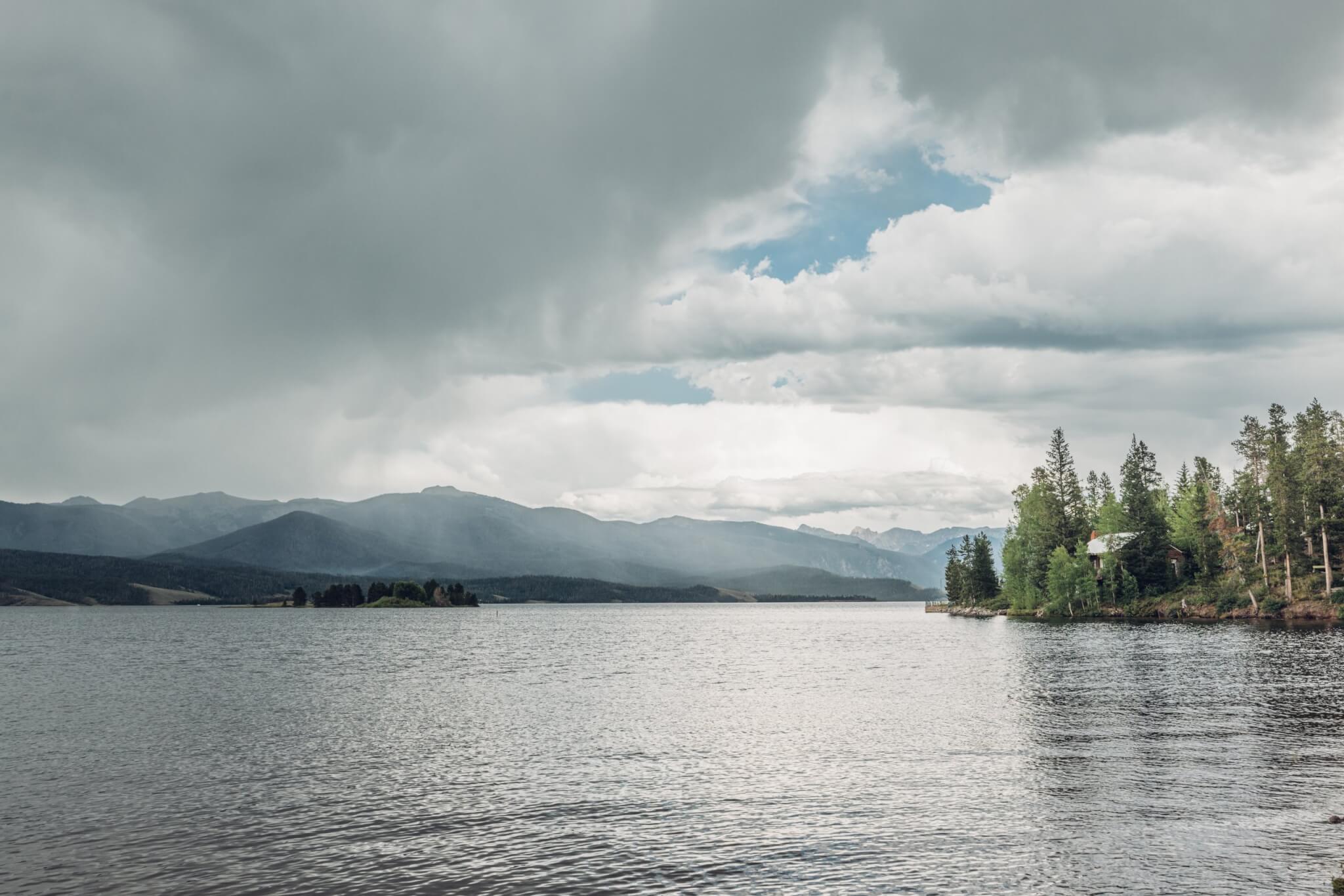 A serene lake with islands, surrounded by mountains and evergreen trees under a cloudy sky in Grand County Colorado.