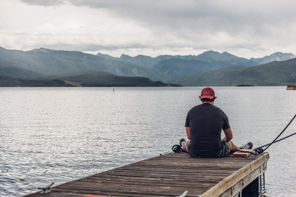 Man sitting on a dock overlooking Granby Lake with mountains in the background.