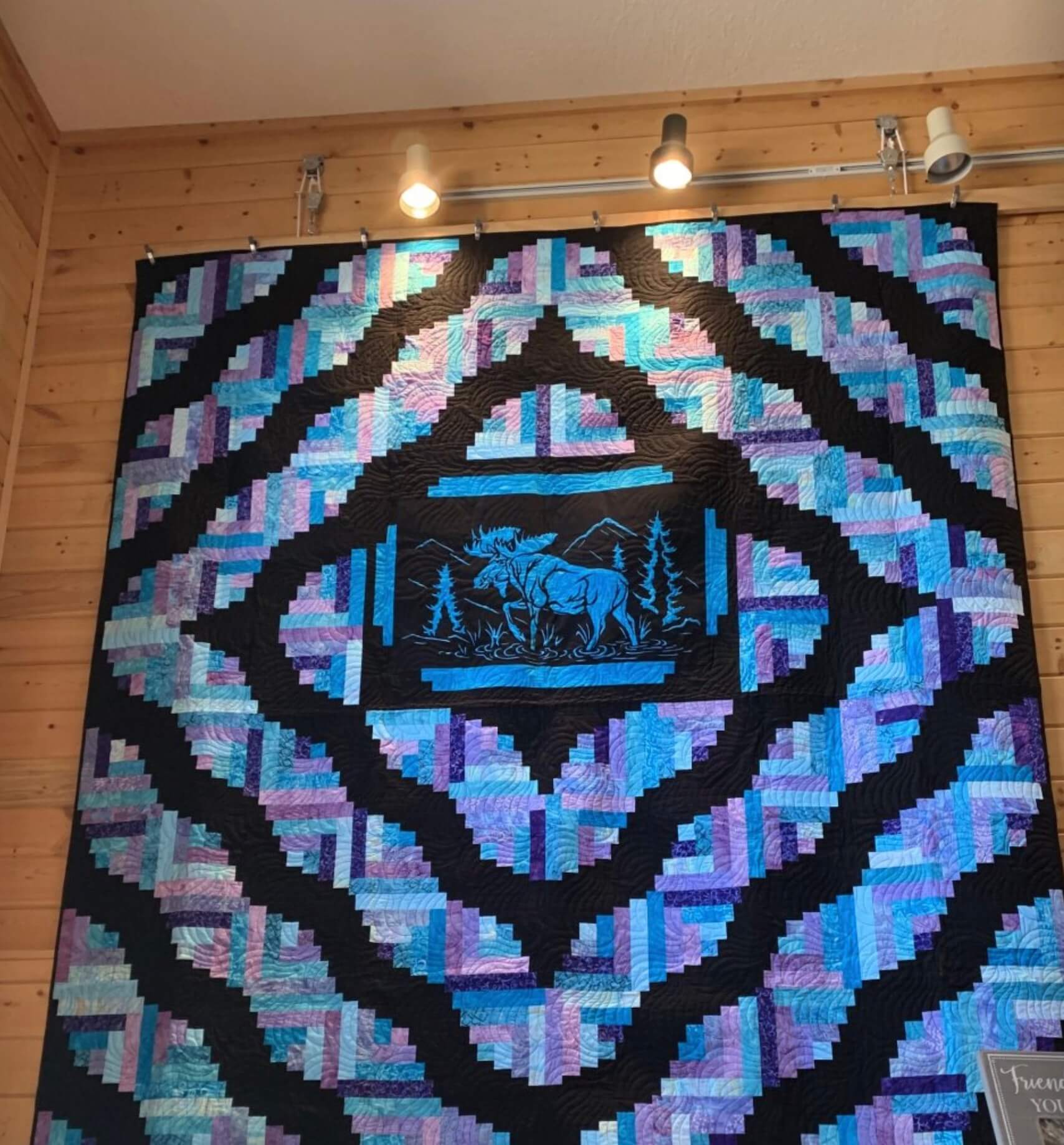 A large, intricately pieced quilt with a moose and trees in the center, hung on a wooden wall in Grand County Colorado.