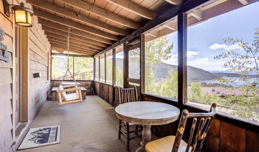 A rustic wooden porch with a round table, chairs, and a swing overlooks a scenic mountain landscape in Grand County Colorado.