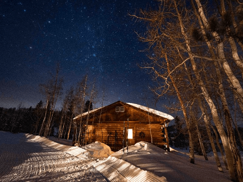 A rustic log cabin nestled in a snowy forest under a starry night sky in Grand County Colorado.