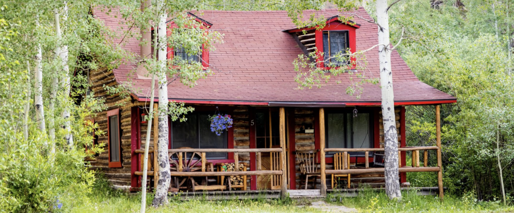 Rustic log cabin nestled in a lush green forest with a red roof and wooden porch in Grand County Colorado.