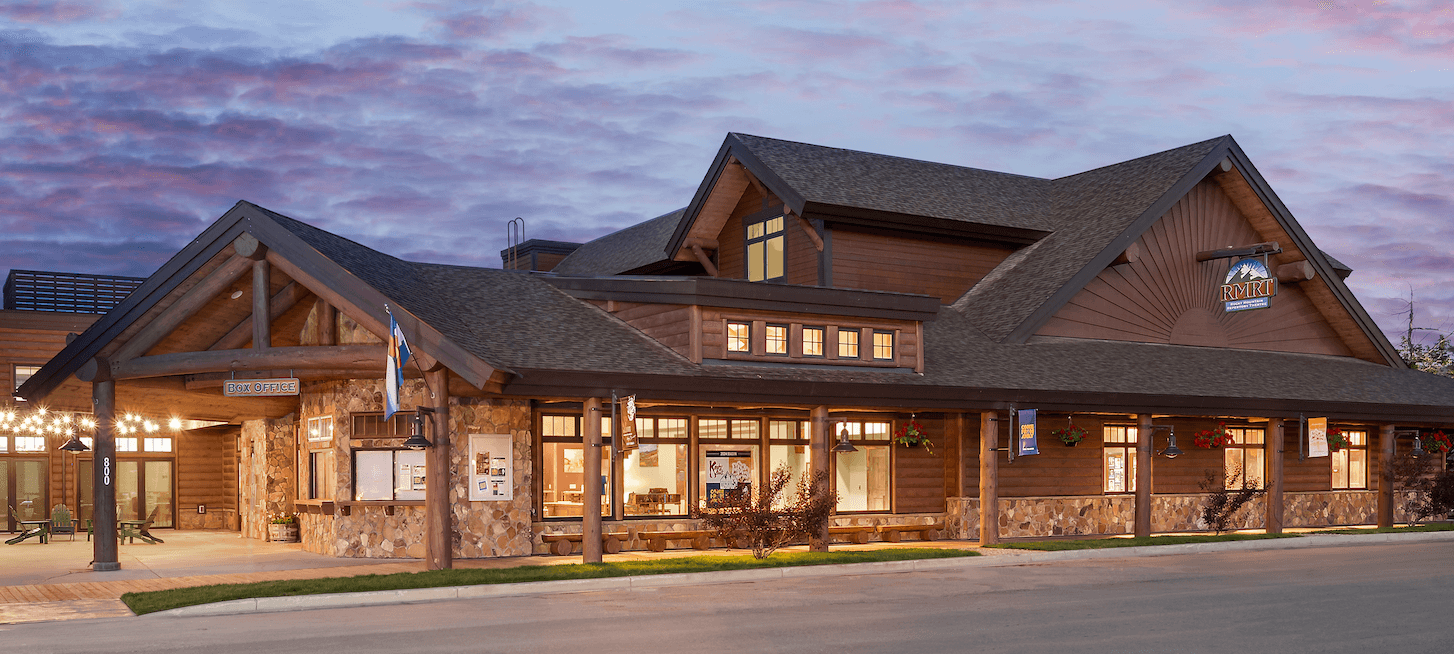 A rustic wooden building with a stone foundation and a large porch, illuminated at dusk in Grand County Colorado.