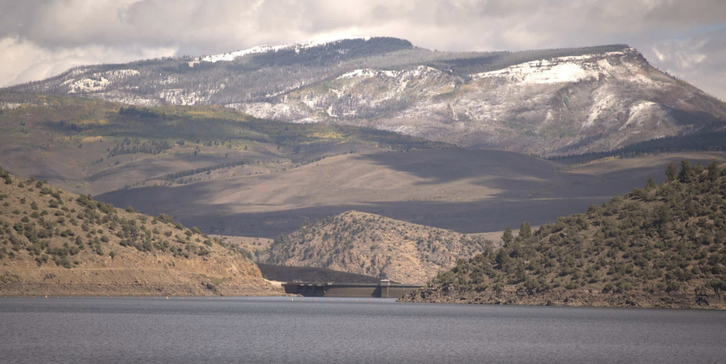 View of Williams Fork Reservoir with rolling hills and snow-dusted mountains in the background.